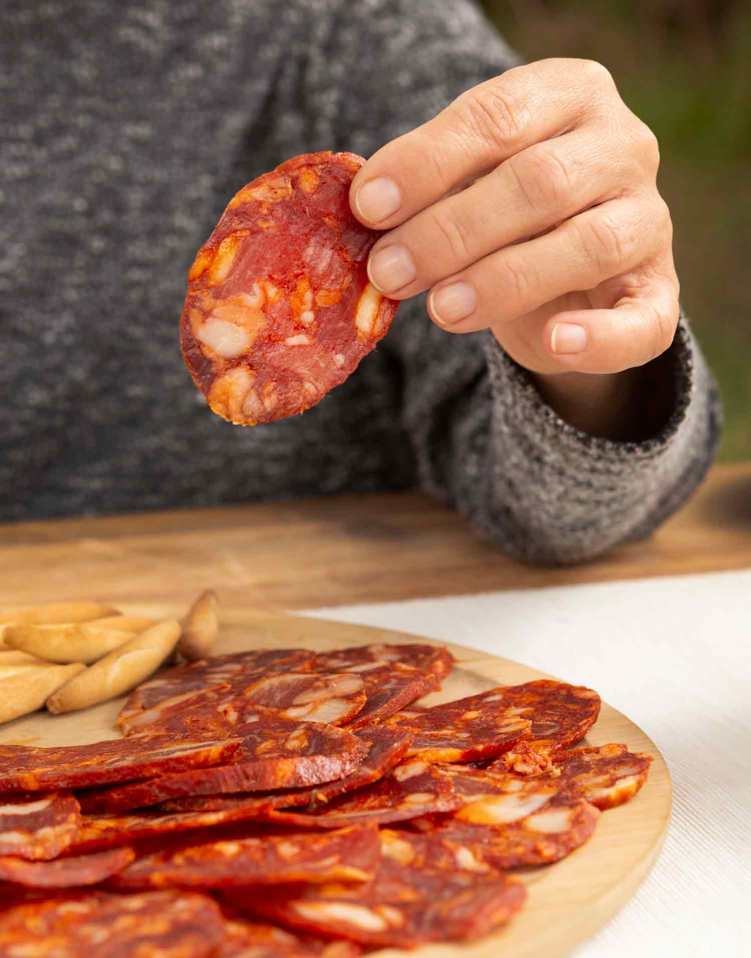 Persona sosteniendo una loncha de chorizo en primer plano sobre una mesa con m&aacute;s chorizo loncheado